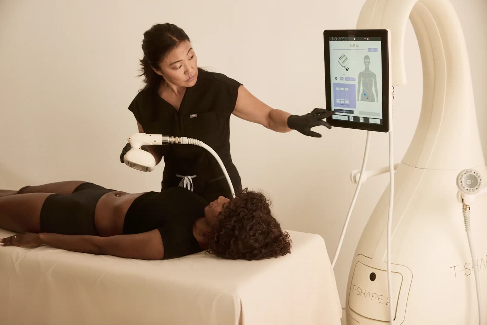 A practitioner adjusting settings on the T-Shape 2 touchscreen beside a client on the table.